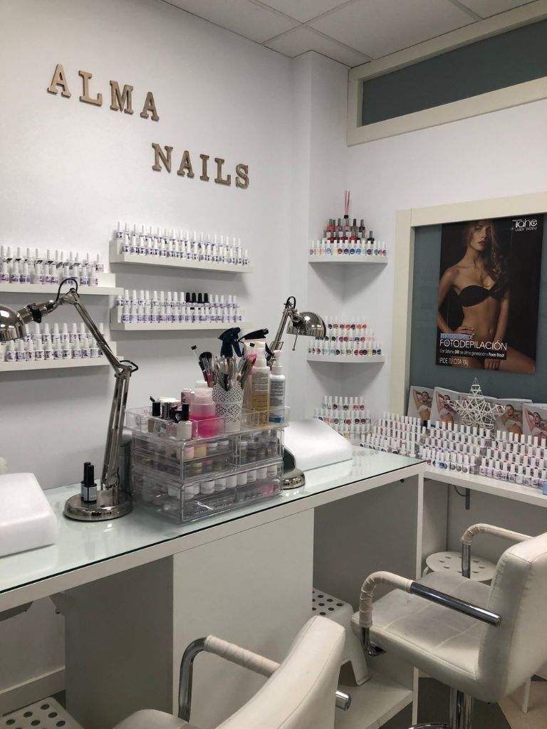 Interior del salón Alma Nails con estantería de productos de belleza y sillones profesionales